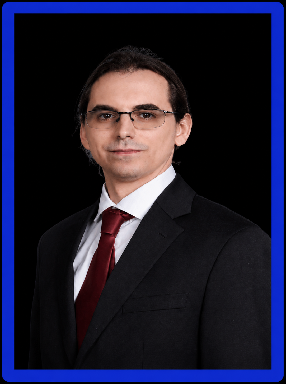 Professional portrait of Shane Pogue wearing glasses, a black suit, white shirt and burgundy tie, against a black background with a royal-blue frame.